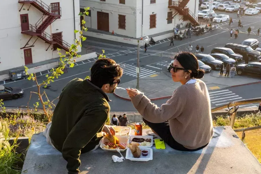 Una pareja cena al aire libre en el centro Fort Mason de San Francisco. La mujer le da de comer a su acompañante.