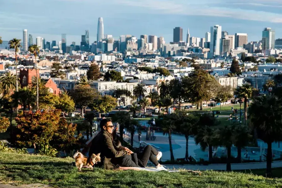 A man and woman sit in an embrace at Dolores Park while gazing at the San Francisco skyline. 