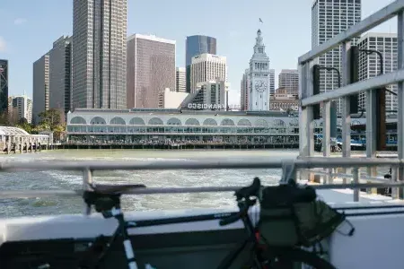 Bicicleta apoyada en una barandilla con el Ferry Building al fondo.