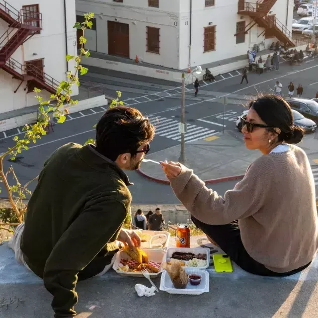 Una pareja cena al aire libre en el centro Fort Mason de San Francisco. La mujer le da de comer a su acompañante.