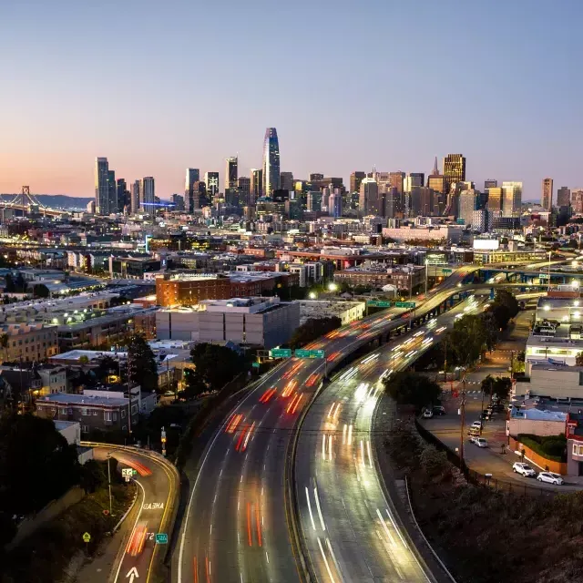 Downtown San Francisco skyline at dusk, with cars rushing on freeway heading in and out of the city.